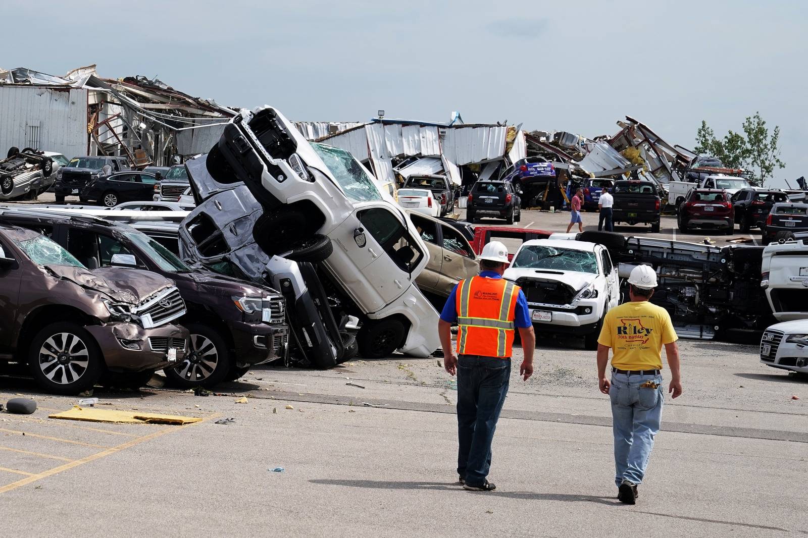 Workers walk past wrecked trucks at a Toyota dealer following a tornado in Jefferson City