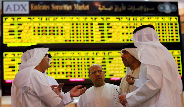 FILE PHOTO: Investors speak in front of a screen displaying stock information at the Abu Dhabi Securities Exchange