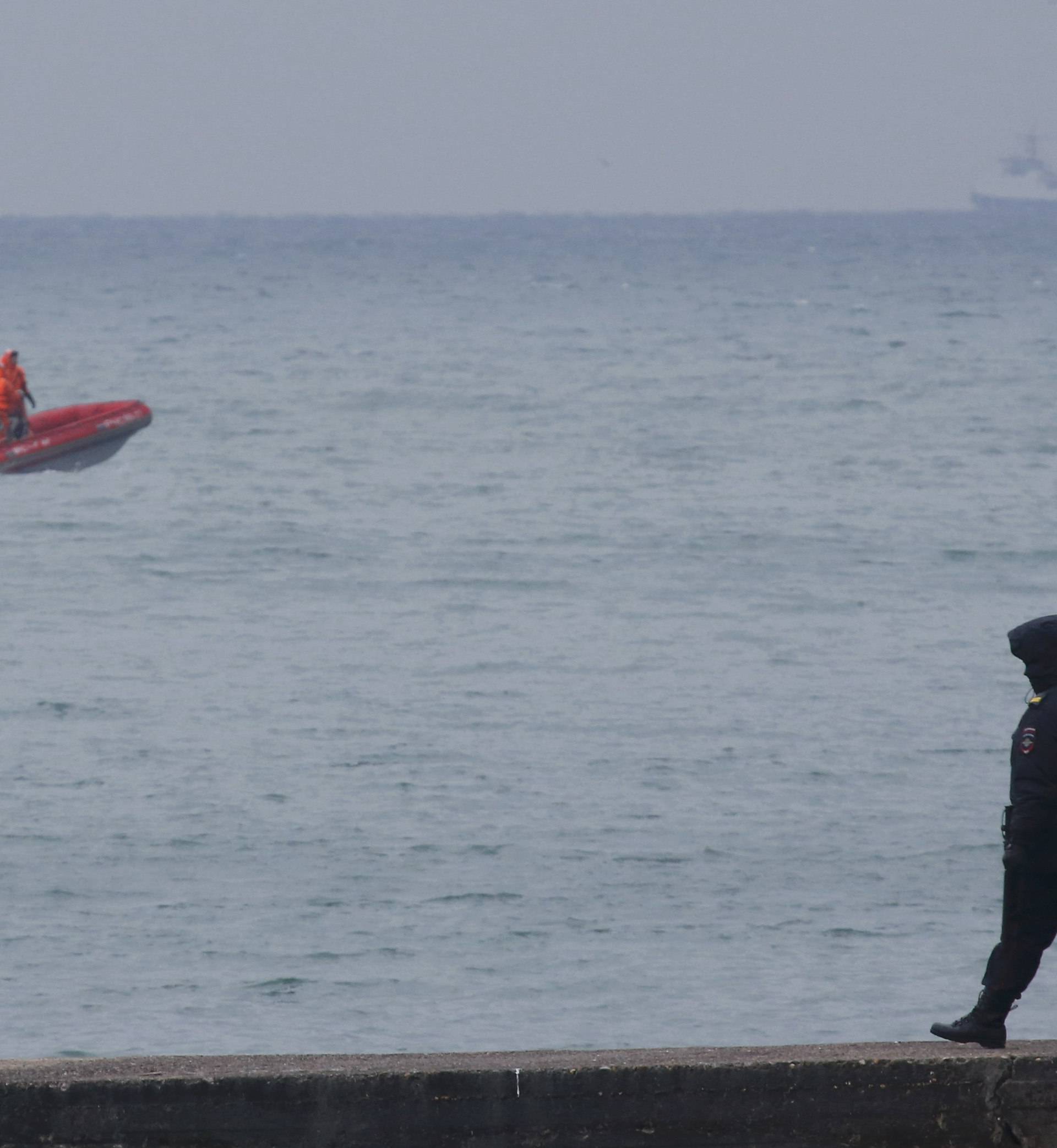 Police officer walks on pier as boat of Russian Emergencies Ministry sails near crash site of Russian military Tu-154 plane in Black Sea in Sochi suburb of Khosta