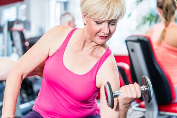 senior woman working out with dumbbells at the gym