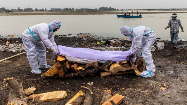 Men wearing protective suits place a white cloth over the body their relative, who died from the coronavirus disease (COVID-19), before his cremation on the banks of the river Ganges at Garhmukteshwar