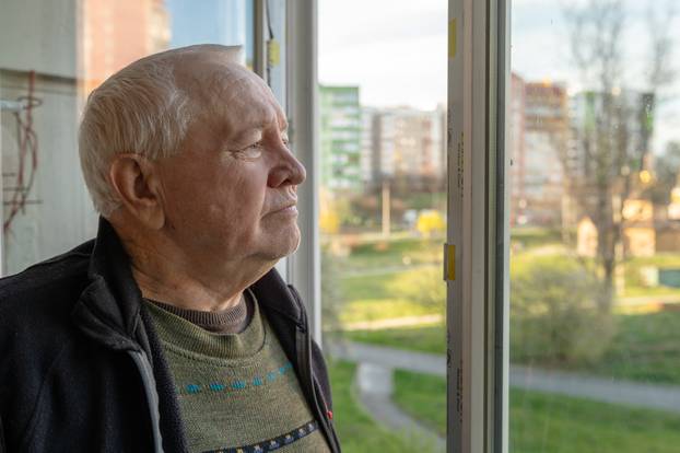 Portrait of a sad elderly man looking out the window at home. Lo