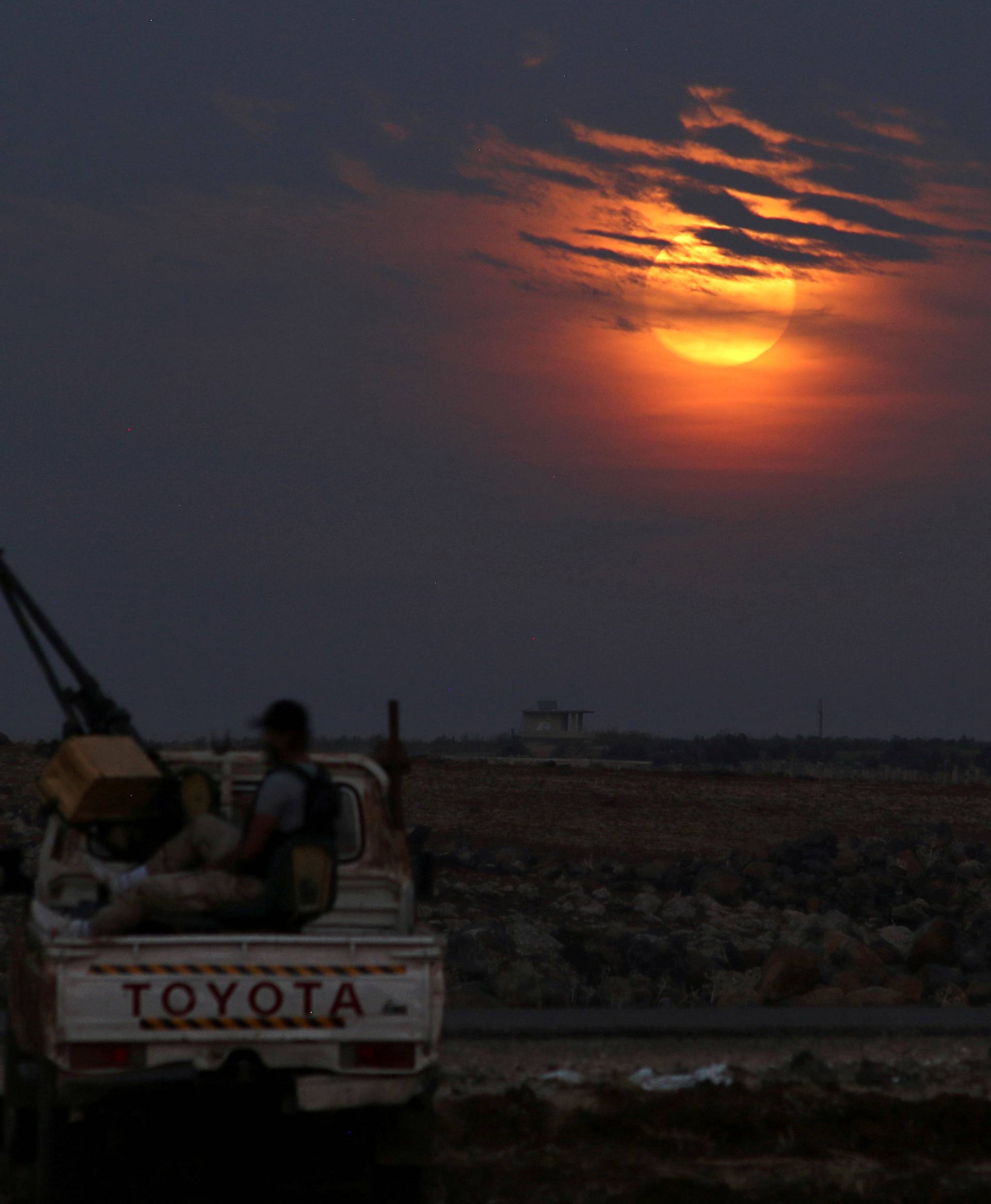 FILE PHOTO: A Free Syrian army fighter sits on a pick-up truck mounted with a weapon, as the supermoon partly covered by clouds is seen in the background, in the west of the rebel-held town of Dael