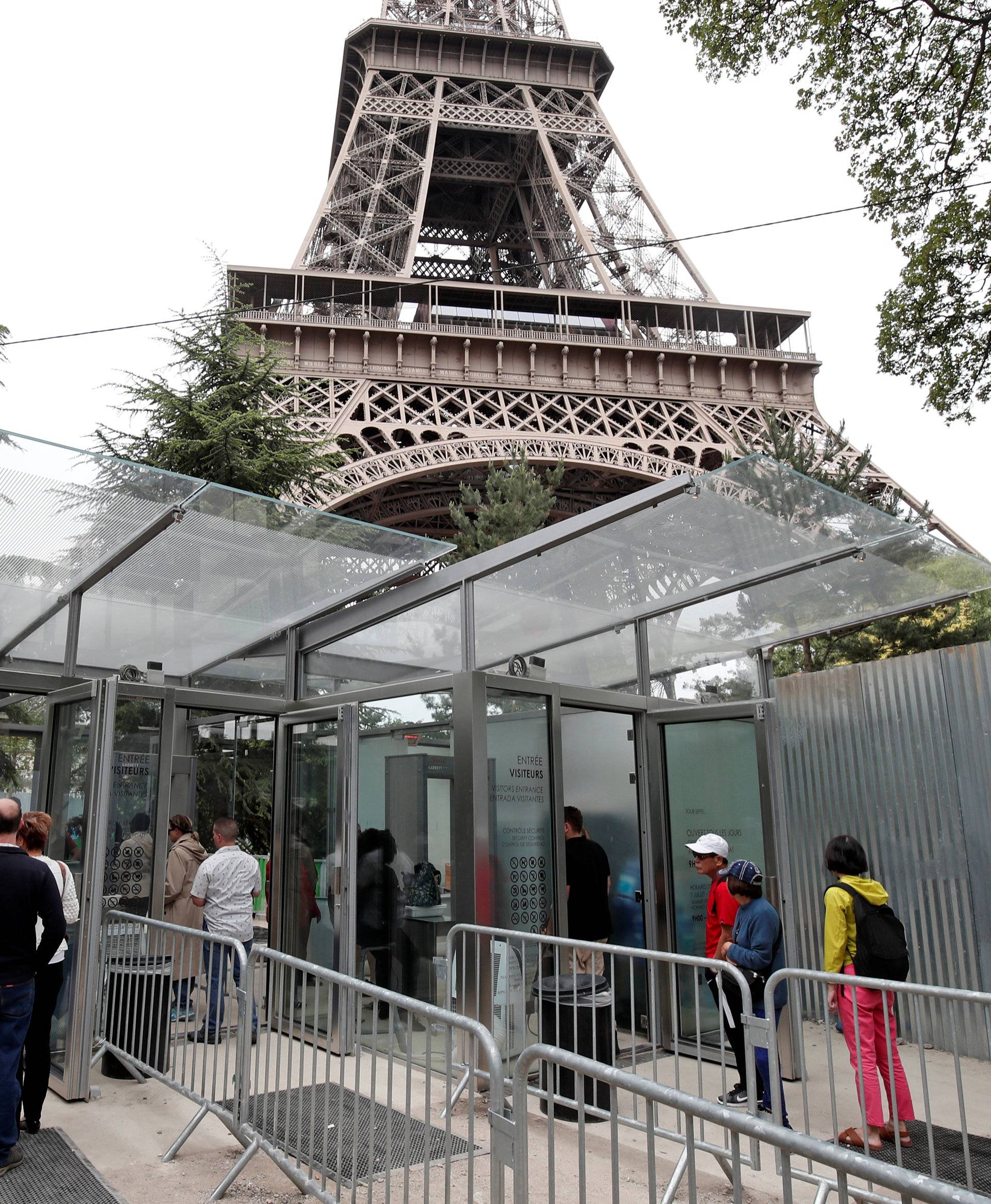 Tourists and visitors queue to pass the security check at the entrance to the new glass fence around the Eiffel Tower in Paris