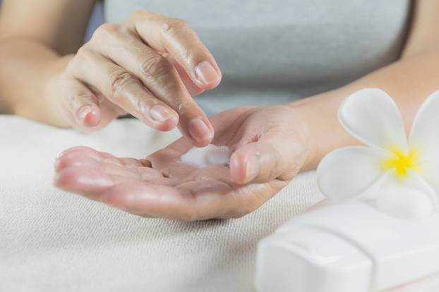 hand of woman apply lotion on skin of hand with lotion bottle on