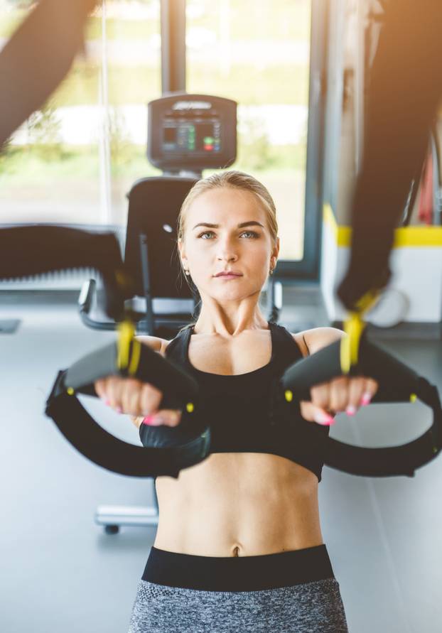 Women training with fitness straps in the gym. Beautiful lady exercising her muscles sling or suspension straps.
