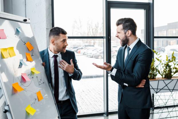 angry businessmen screaming at coworker near white board in modern office