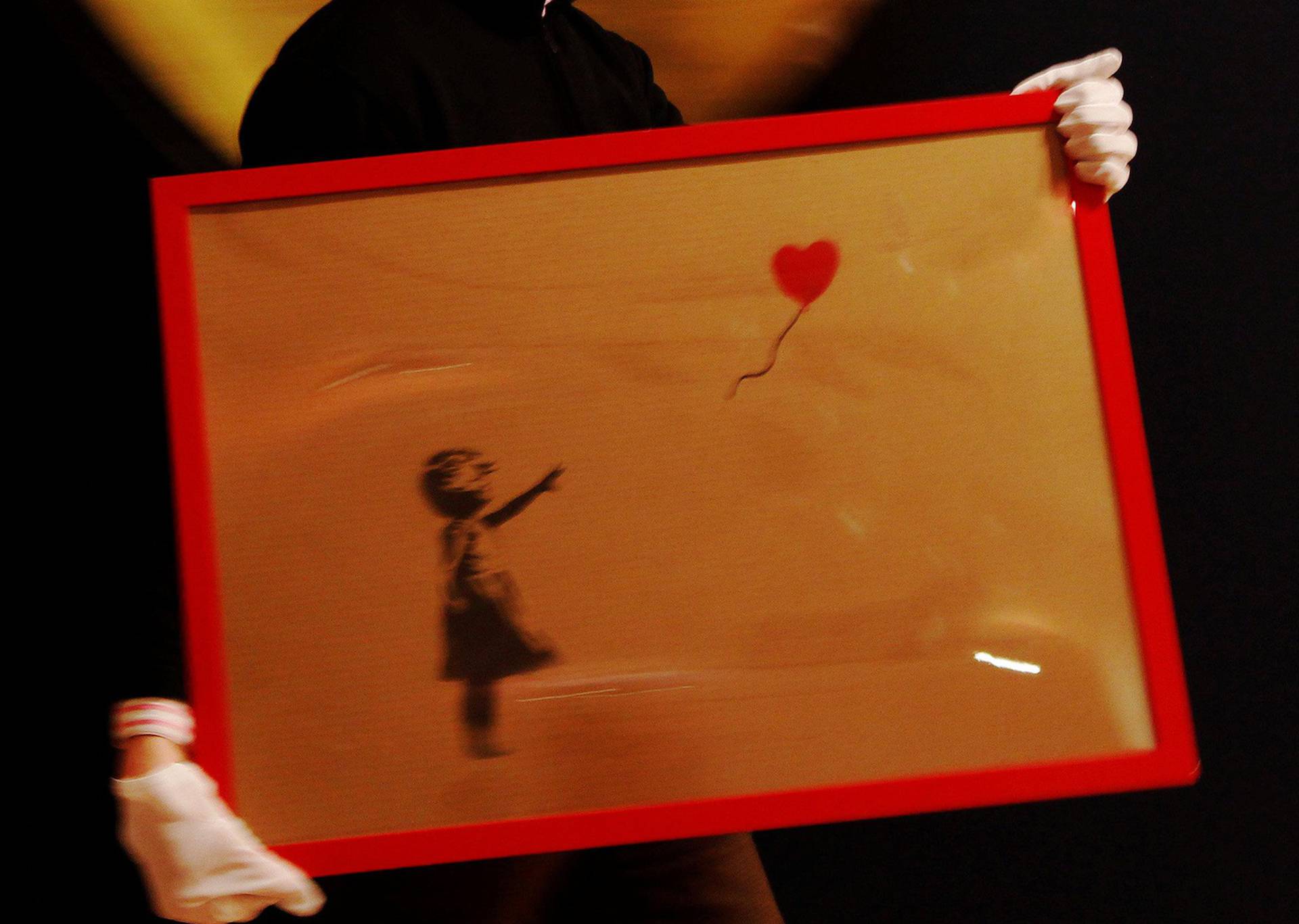 FILE PHOTO: An employee walks with artist Banksy's "Girl and Balloon" 2009 signed and inscribed For Mike, past artist  Ryan Callanan's (known as RYCA) "Mega Heart" 2011 at Bonhams auction house in London