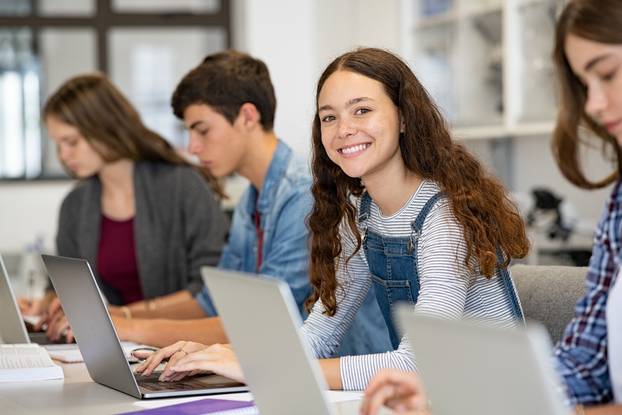 Happy,Young,Woman,Working,On,Laptop,And,Looking,At,Camera