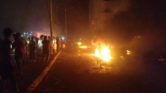 People look at cars on fire at the site of an explosion outside Aden international airport in Aden
