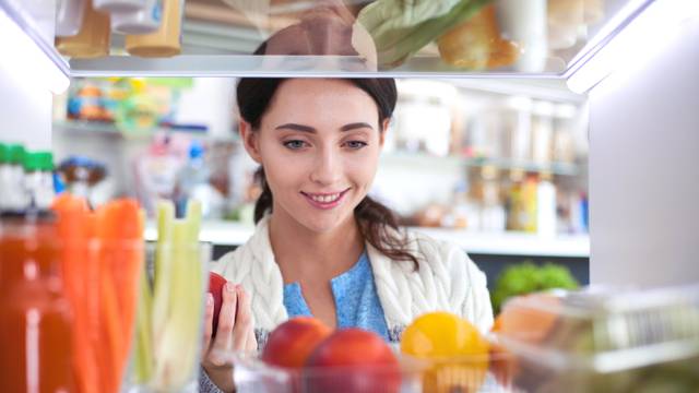 Portrait of female standing near open fridge full of healthy food, vegetables and fruits