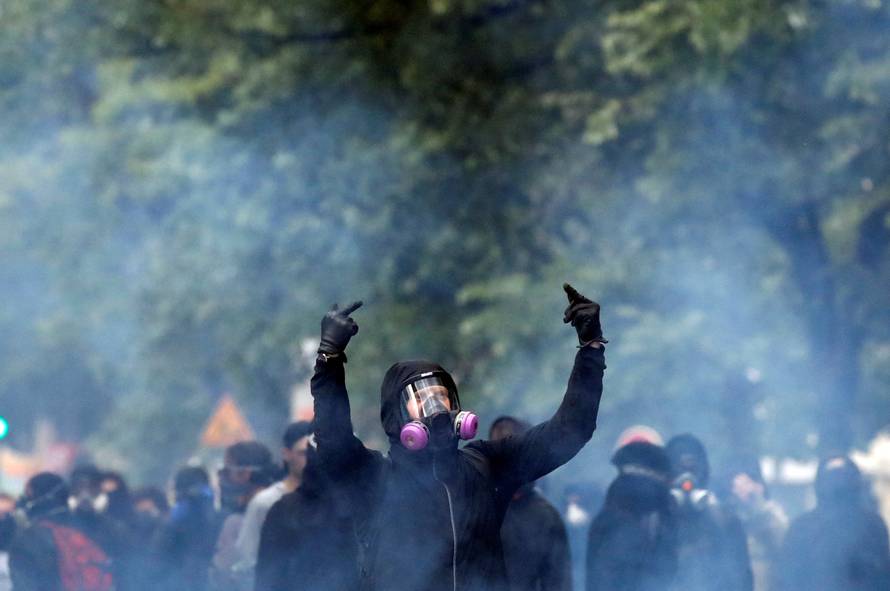 Tear gas floats in the air as a masked protester reacts during clashes with French riot police at the May Day labour union rally in Paris