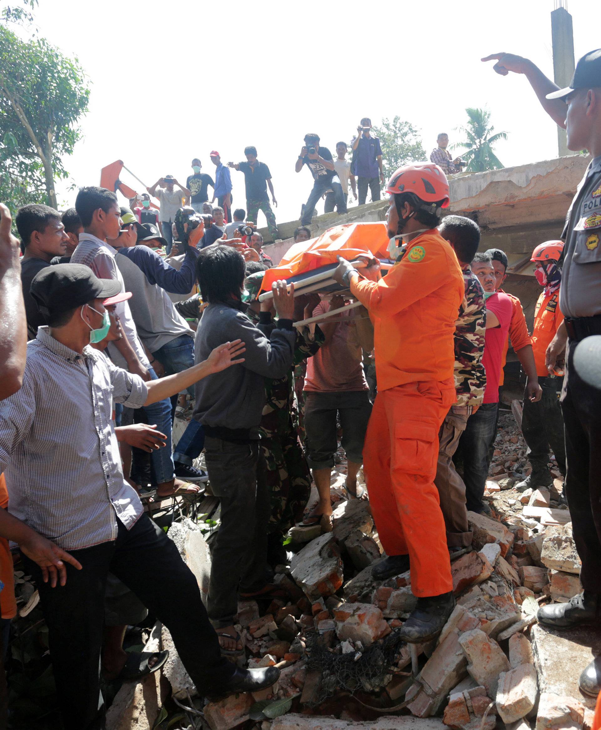 Rescue workers and police remove a victim from a collapsed building following an earthquake in Lueng Putu, Pidie Jaya in the northern province of Aceh, Indonesia