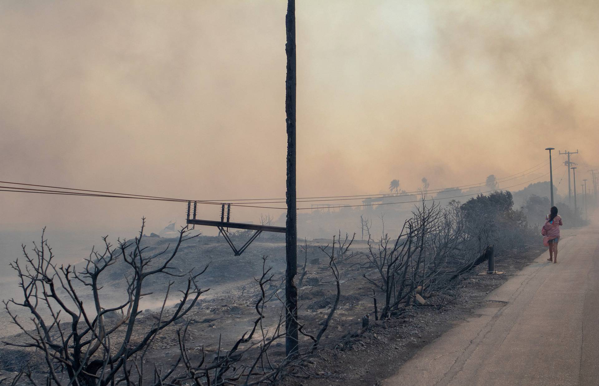 A person walks amidst smoke rising from wildfire burning near Lindos on the island of Rhodes