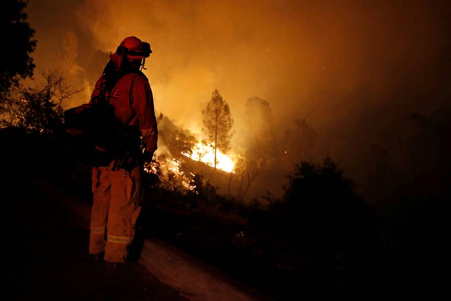 A firefighter watches the flames of the Carr Fire advance as it burns west of Redding