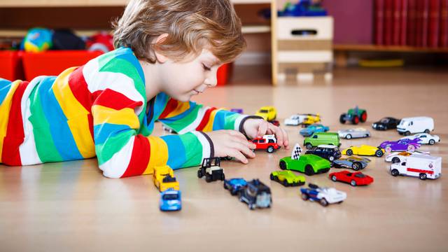 Little blond child playing with lots of toy cars indoor