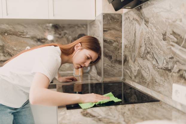A woman is cleaning in the kitchen with a rag in her hands