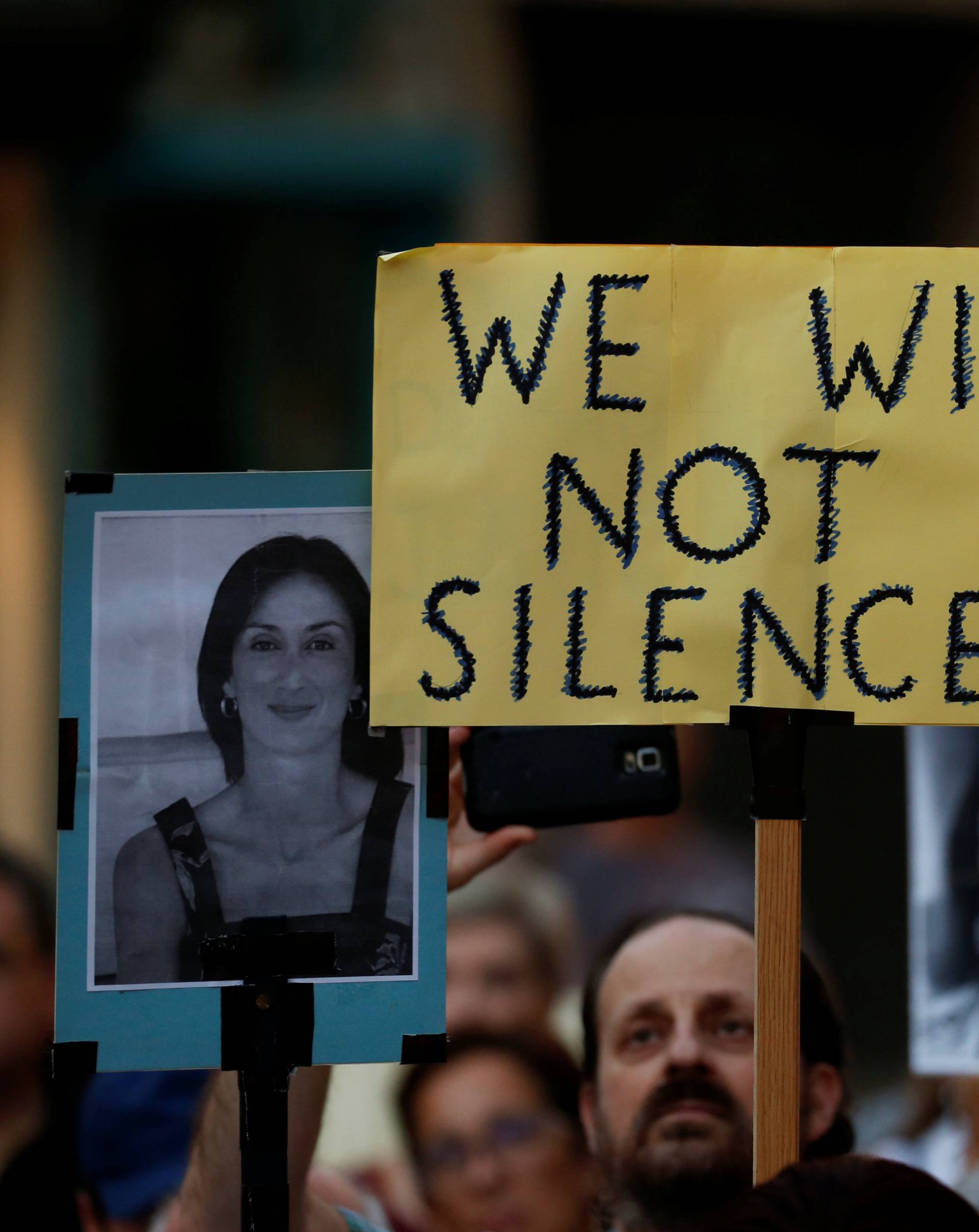 People hold photos of assassinated anti-corruption journalist Daphne Caruana Galizia during a vigil to mark eleven months since her murder in a car bomb in Valletta