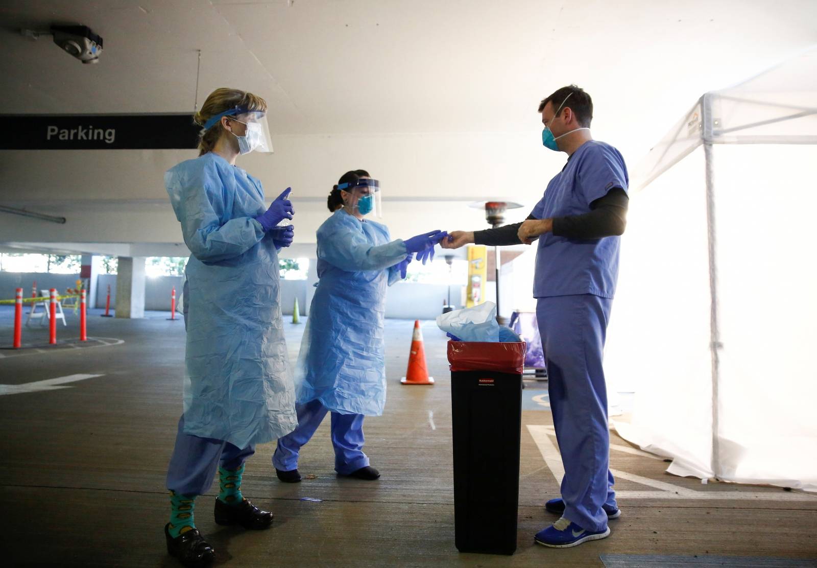 Nurses Barton and White help nurse Gates take off protective gear after interacting with a patient at a drive-through testing site for coronavirus, flu and RSV, currently by appointment for employees at UW Medical Center Northwest