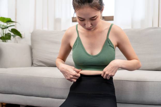 Sporty woman in sportswear hold cellulite on her belly waist and