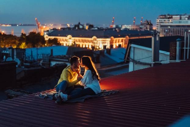 Loving couple is sitting on the roof of the house. Beautiful evening