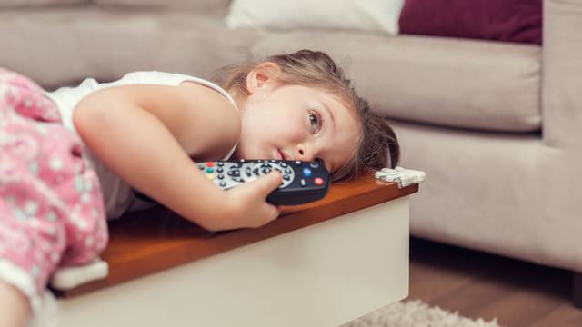 Cute,Little,Girl,With,Remote,Control,Lying,On,Coffee,Table