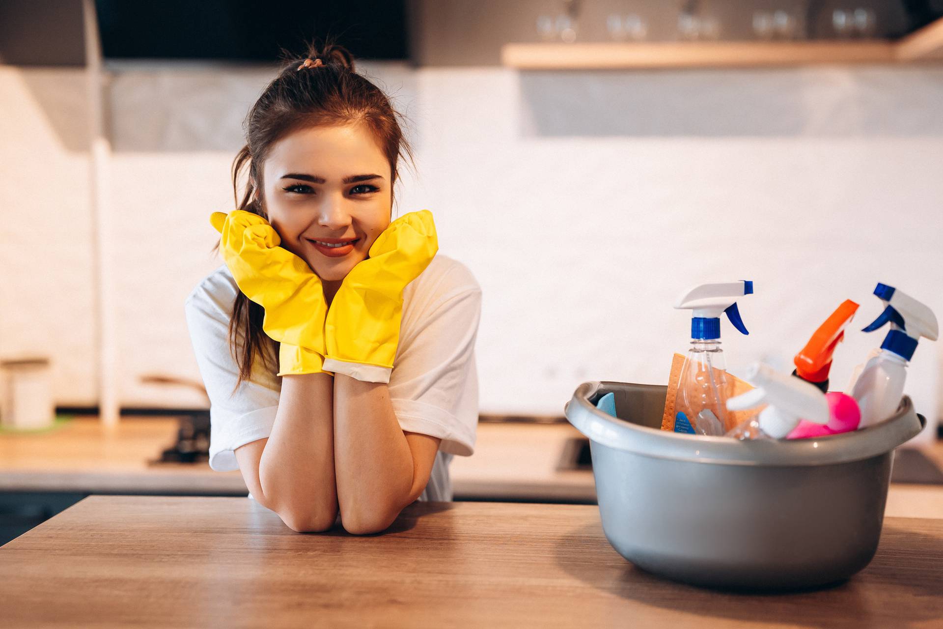 Pretty woman in protective yellow gloves is smiling in the kitchen while cleaning.