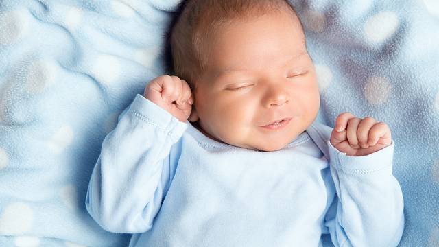Newborn Baby Sleeping Smiling. Cute Infant Child In Wrap Bodysui
