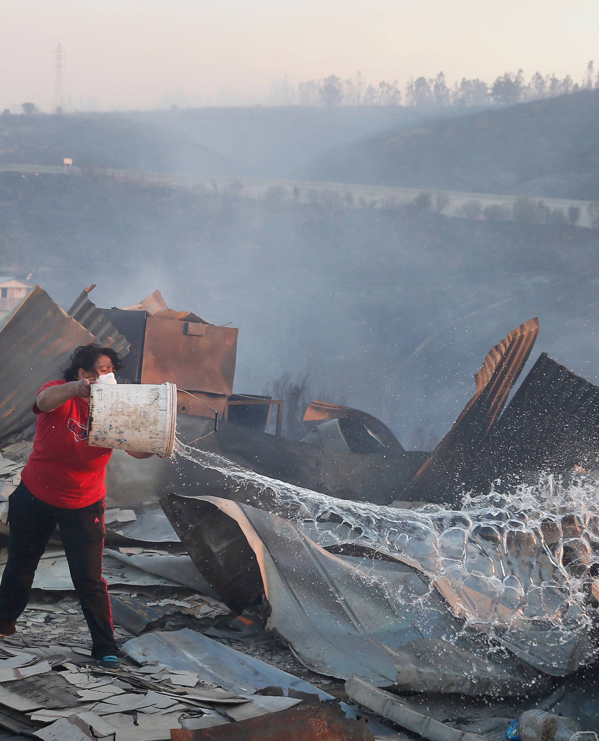 A woman throws water over her burned house on a hill, where more than 100 homes were burned due to a forest fire but there have been no reports of death, local authorities said in Valparaiso, Chile