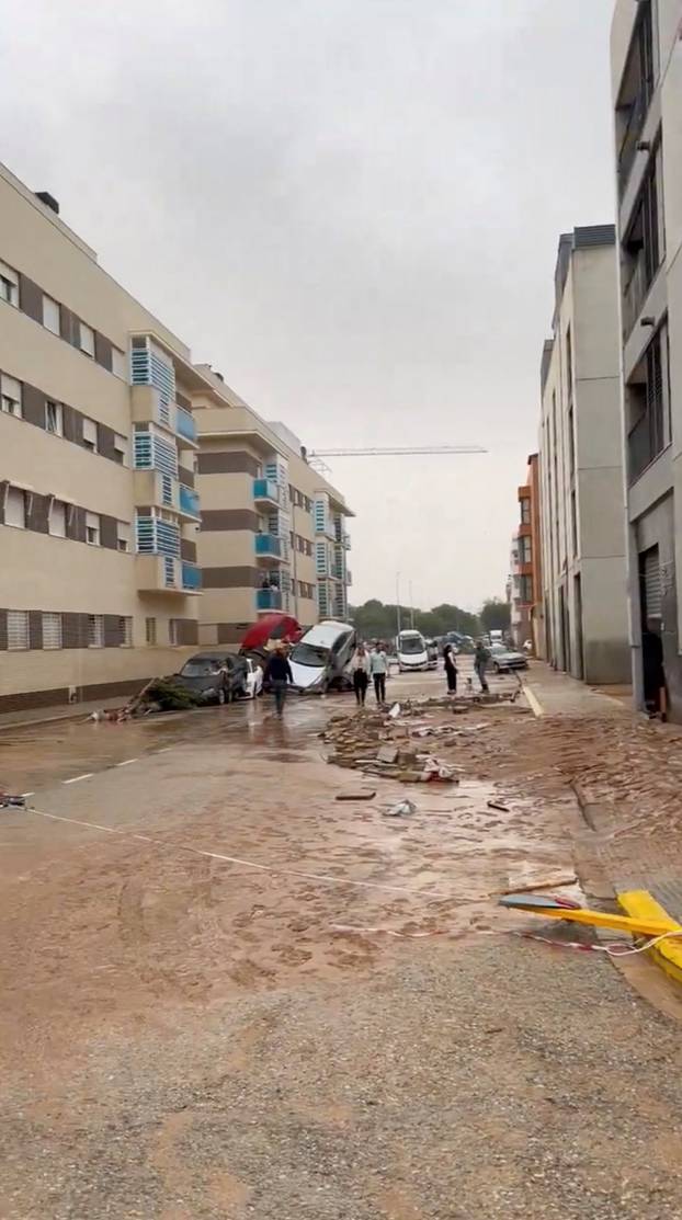 People walk past damaged vehicles piled up after torrential rains and flooding in Paiporta, Valencia