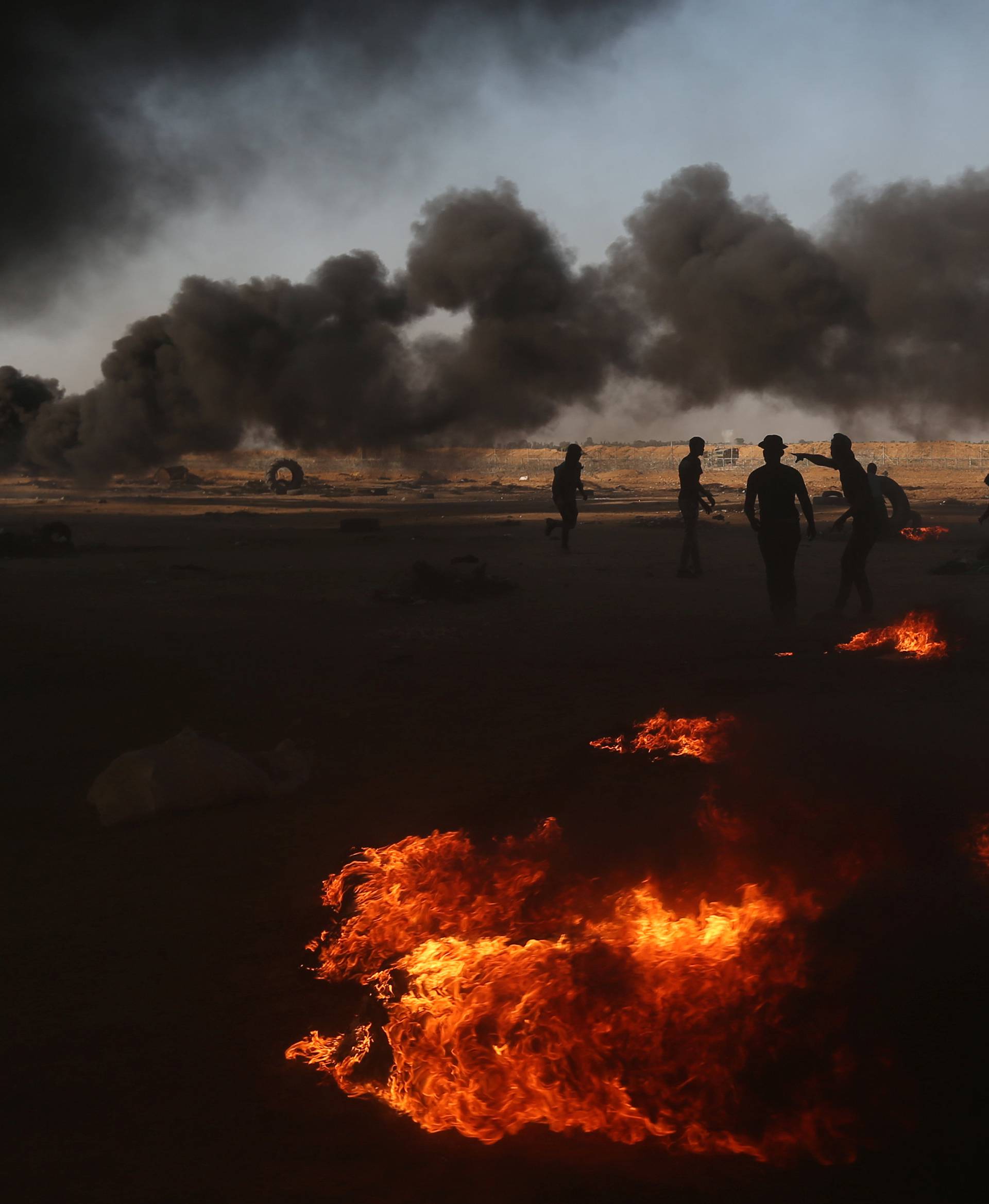Palestinian demonstrators are seen as smoke rises from burning tires during a protest marking the 70th anniversary of Nakba, at the Israel-Gaza border in the southern Gaza Strip