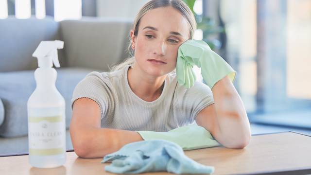 Woman, tired and burnout after cleaning house, office or home with spray, chemical or sanitizer. Cleaner, gloves and table for domestic work, job or service take time to rest, breathe and relax