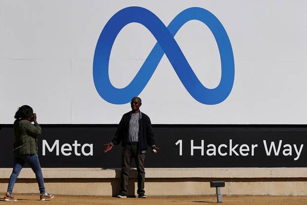 FILE PHOTO: A man poses in front of a sign of Meta, the new name for the company formerly known as Facebook, at its headquarters in Menlo Park