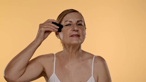 Elderly Woman Using Gua Sha Tool for Facial Massage Therapy