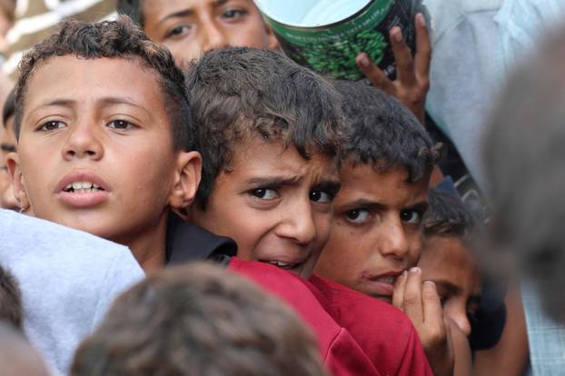 Palestinians gather to receive meals cooked by a charity kitchen, in Deir Al-Balah, central Gaza Strip