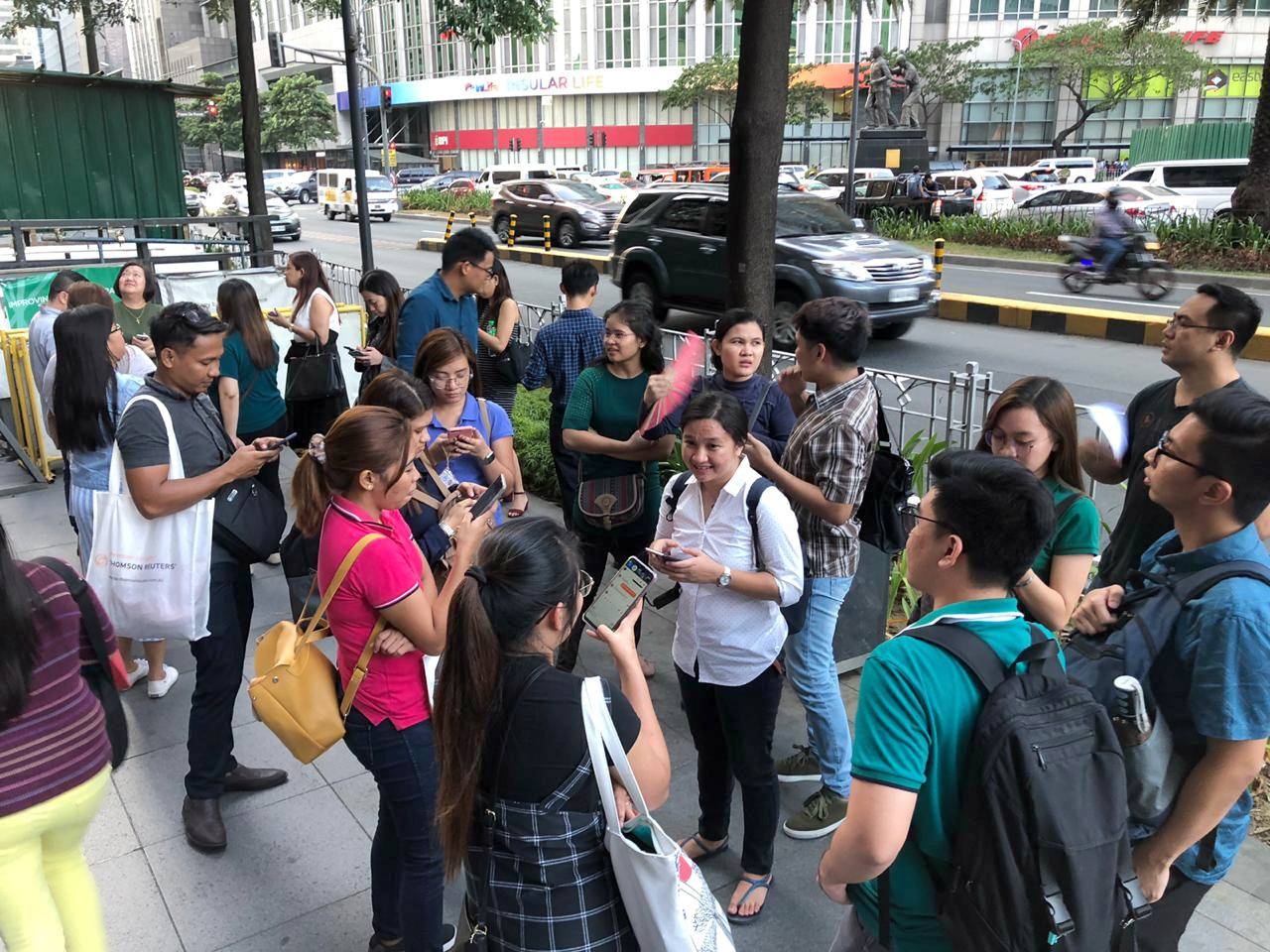 Employees wait outside after being evacuated from the office building after an earthquake in Makati City