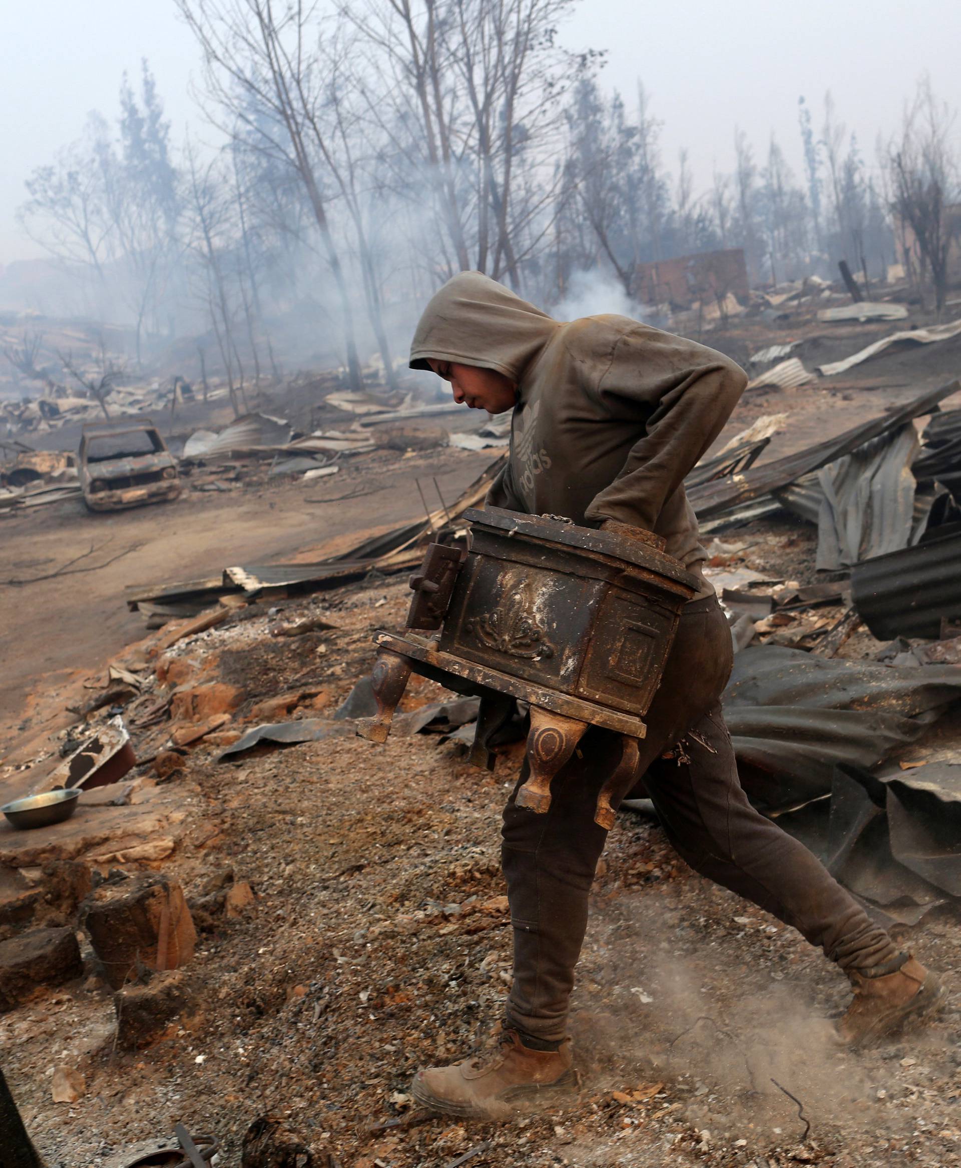 A man carries a stove while walking through the remains of a burnt house as the worst wildfires in Chile's modern history ravage wide swaths of the country's central-south regions, in Santa Olga