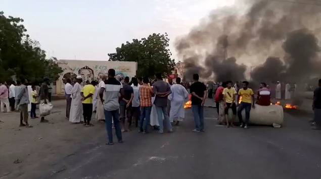 People gather around as smoke and fire are seen on the streets of Kartoum, Sudan, amid reports of a coup
