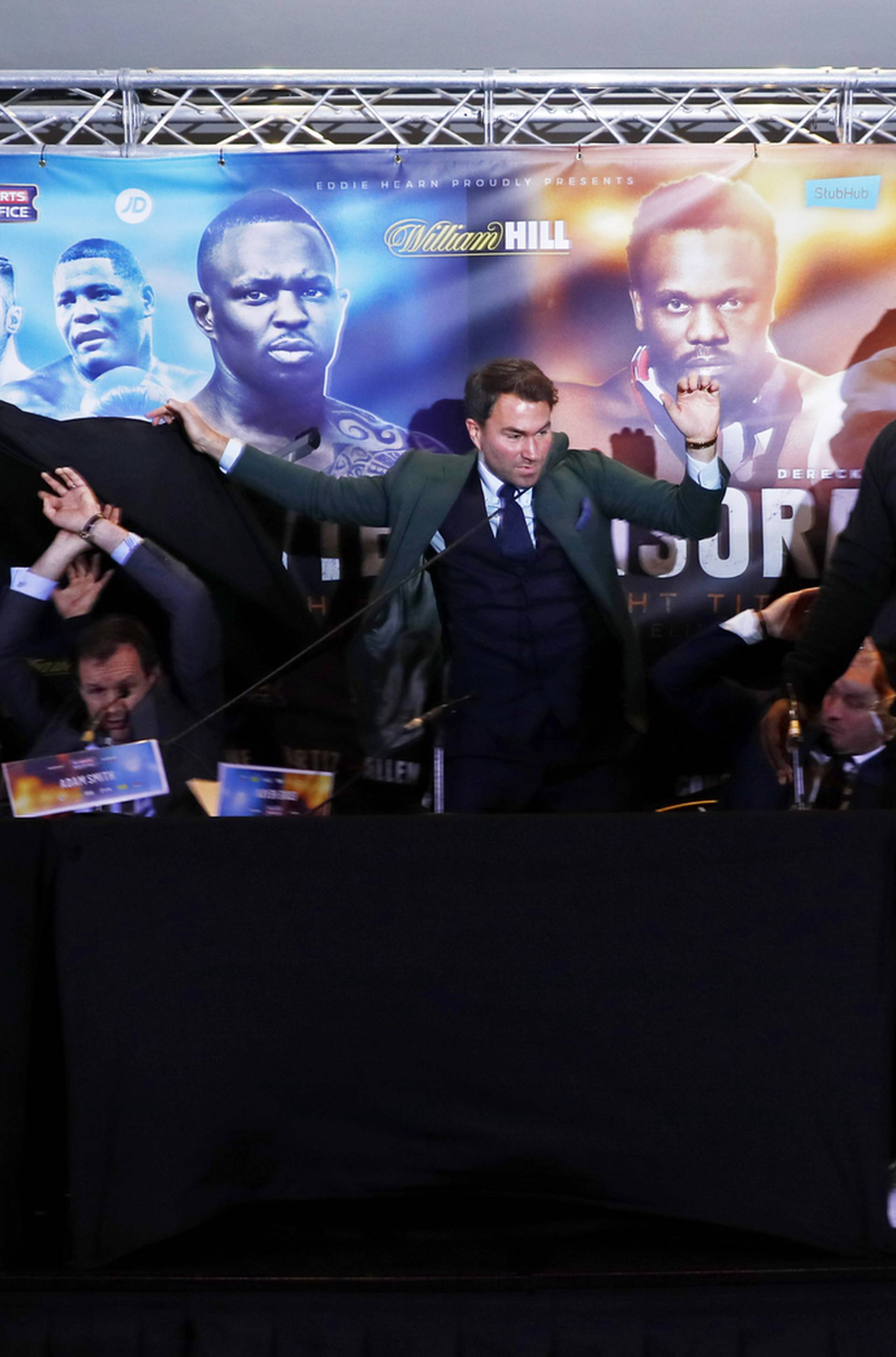 Dillian Whyte, trainer Mark Tibbs, Sky Sports' Adam Smith, promoter Eddie Hearn and promoter Kalle Sauerland look on as Dereck Chisora throws a table during the press conference