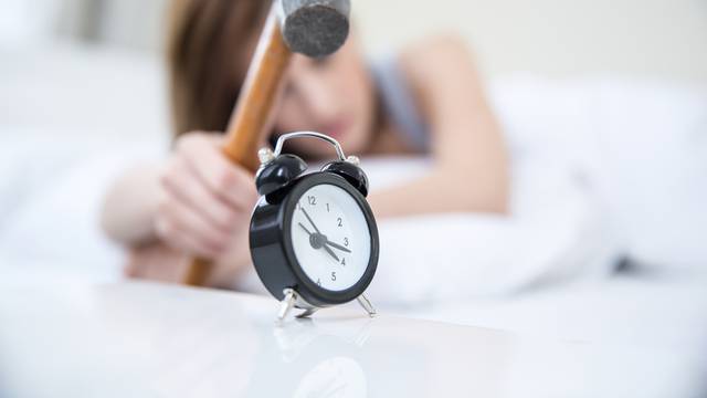 Woman not wanting to get up, taking a hammer to her alarm clock. Focus on clock