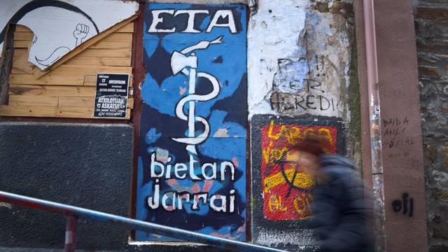 A woman walks past a mural depicting the serpent and axe emblem of armed Basque separatists ETA in Bermeo