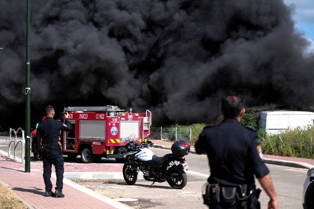 Israeli policemen stand next to smoke from a fire following incoming rockets from Lebanon to Israel in Bezet