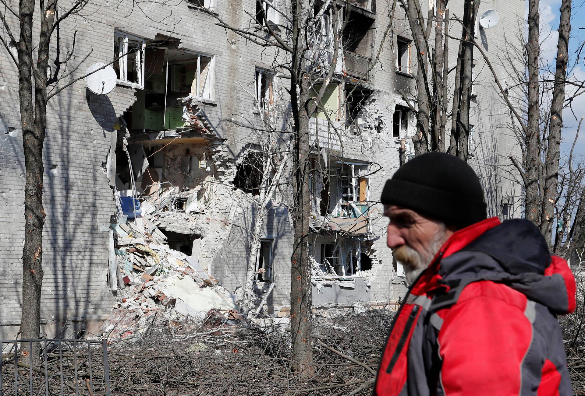 A local resident stands next to a damaged residential building in Volnovakha