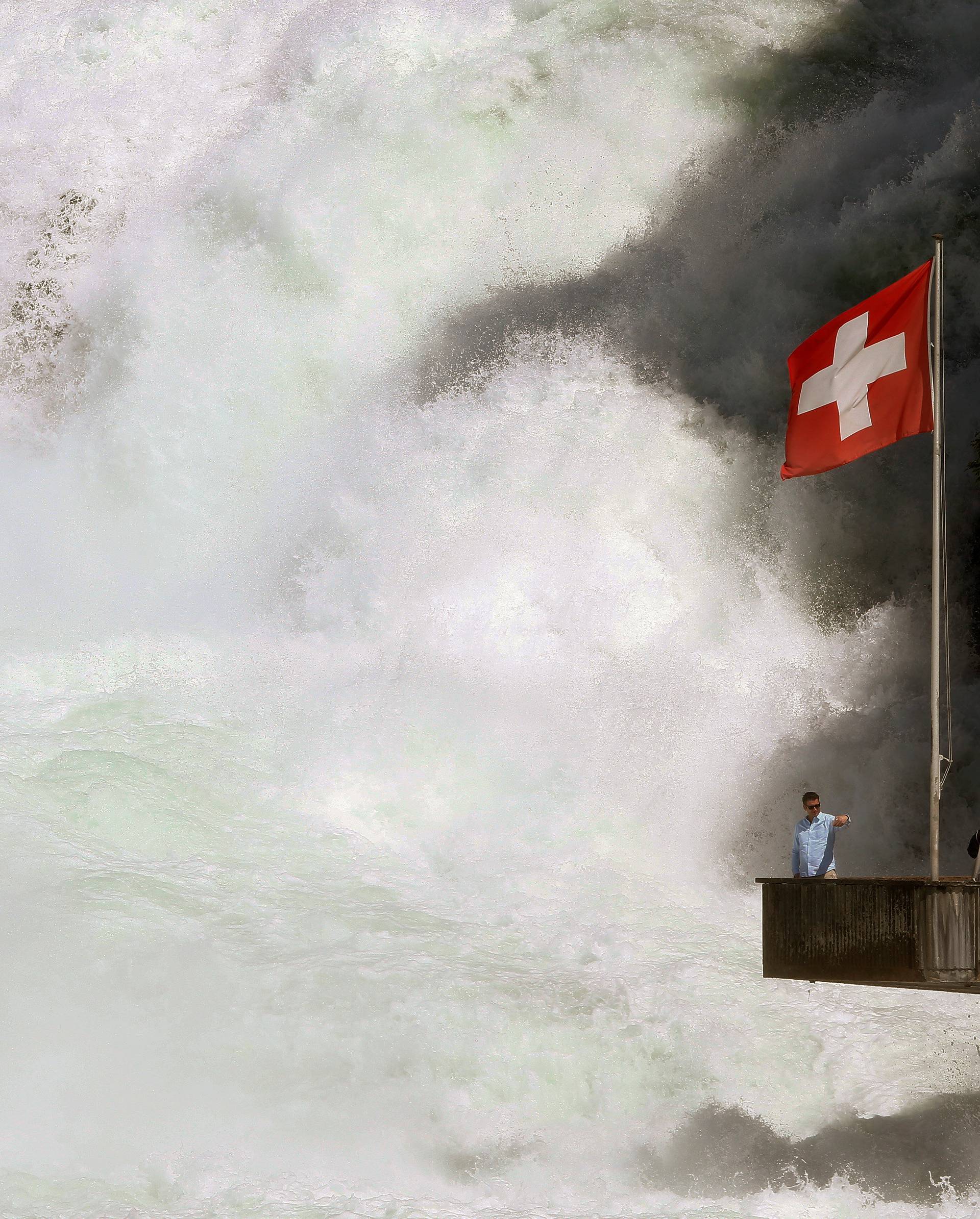 Switzerland's national flag fies as a man takes a selfie on a visitor platform beside the Rhine Falls in Neuhausen