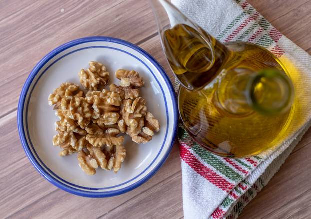 Healthy peeled nuts on a ceramic plate accompanied by a bottle of extra virgin olive oil. Top view.