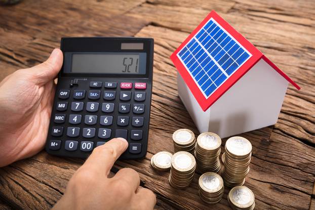 Businessman,Using,Calculator,By,Coins,And,Model,Home,With,Solar