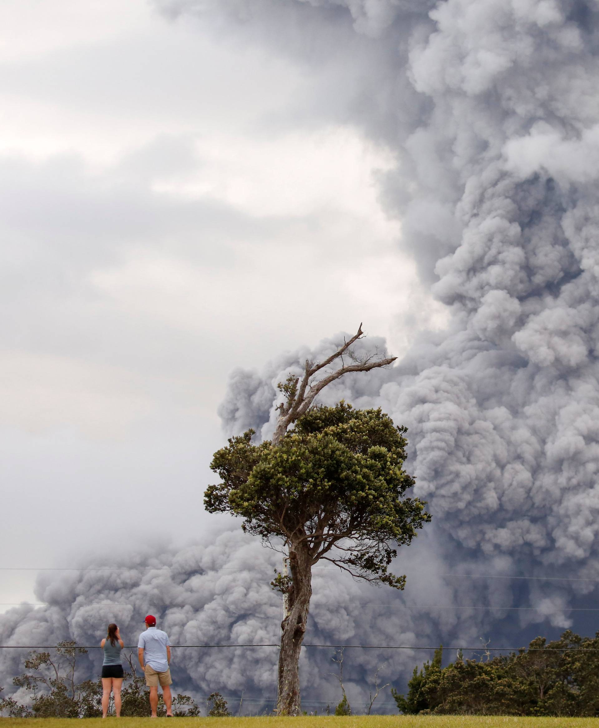 People watch as ash erupt from the Halemaumau crater near the community of Volcano