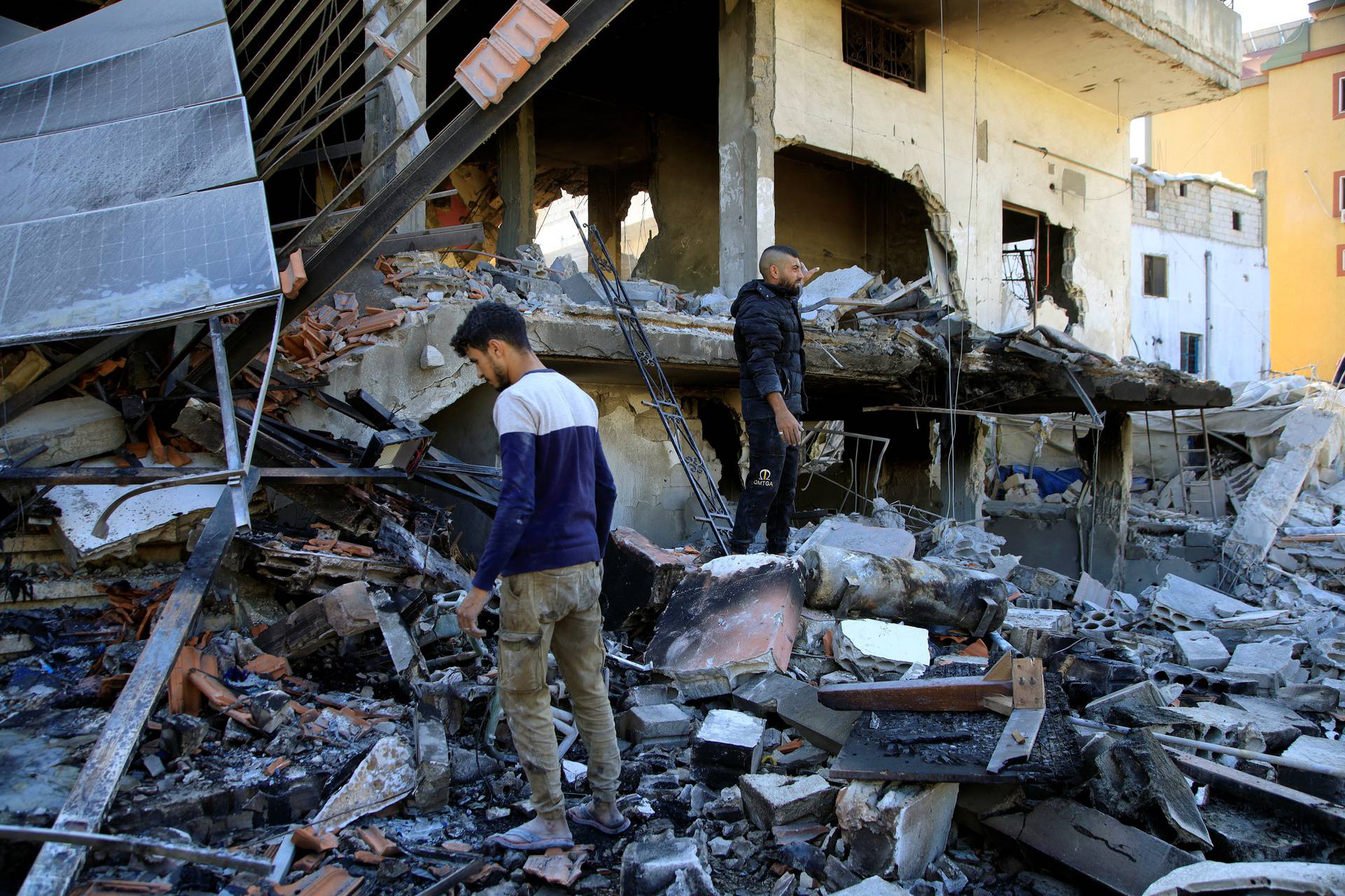 People stand on the rubble of a damaged building, in Akbiyeh