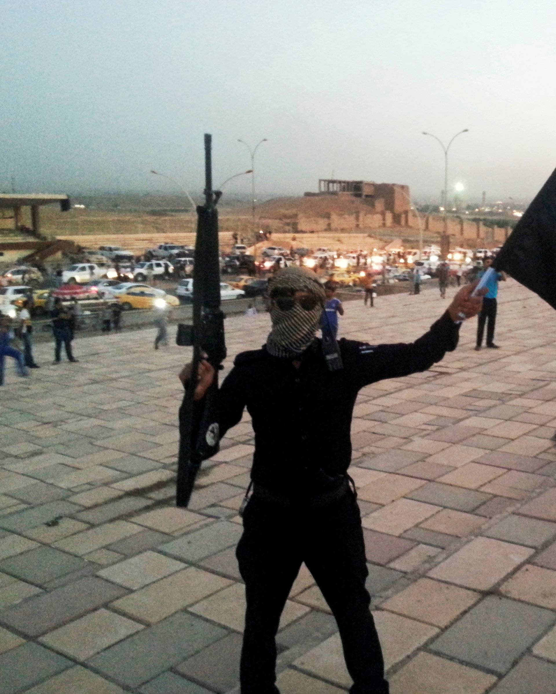 A fighter of ISIL holds a flag and a weapon on a street in Mosul