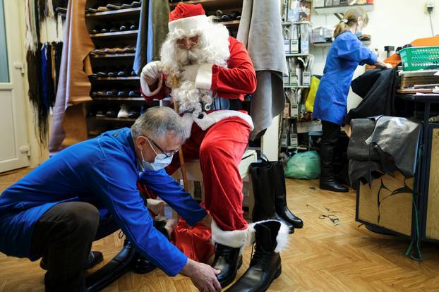Romanian cobbler Grigore Lup ties the laces of a pair of oversized winter boots worn by Santa Claus impersonator Claudiu Dascal